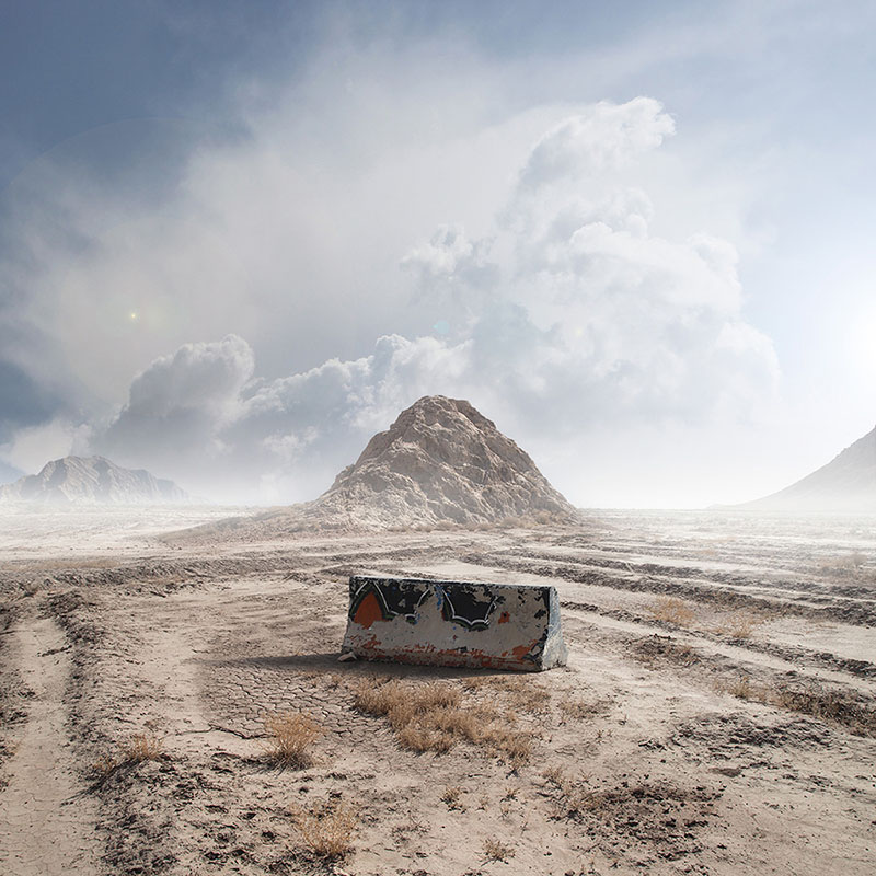 Color version: a concrete barrier in a desert plain below a mountain and storm clouds