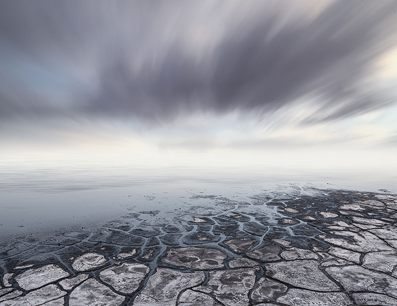 Long-exposure seascape with streaking storm clouds over cracked salt flats