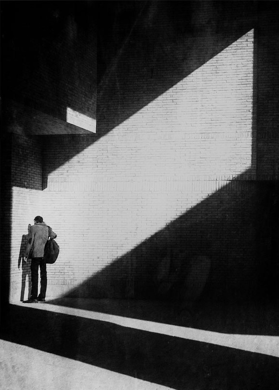 Crop A: a tight vertical crop of a man in a diagonal band of light against a brick wall