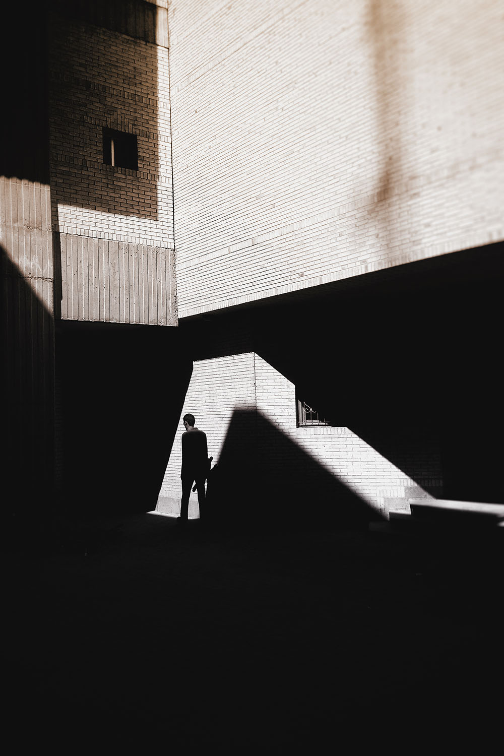 A small figure in a sliver of light between dark concrete buildings