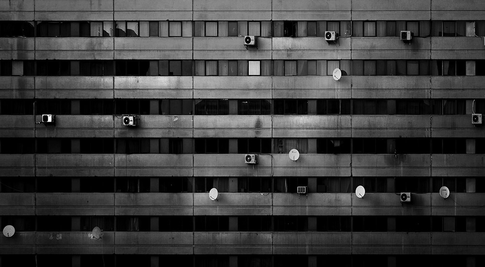 Black-and-white facade of a concrete apartment block with rows of windows, air conditioners and satellite dishes
